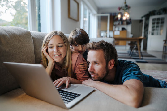 Happy family lying on couch, using laptop