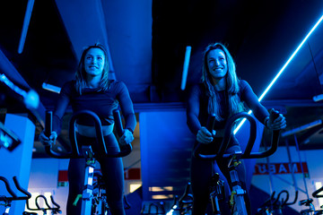 Smiling twin sisters exercising on spinning bikes in gym