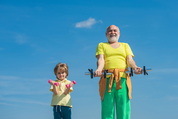 Cute kid and senior man exercising with dumbbells. Sports coach and kid building strength with dumbbells.