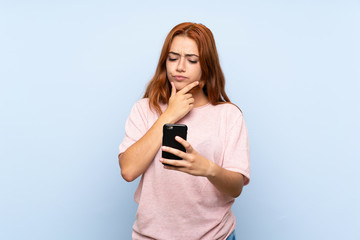 Fototapeta premium Teenager redhead girl over isolated blue background thinking and sending a message