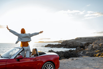 Woman enjoying beautiful view on the ocean, sitting with raised hands on the convertible car during...