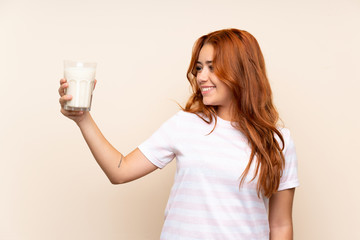 Teenager redhead girl holding a glass of milk over isolated background with happy expression