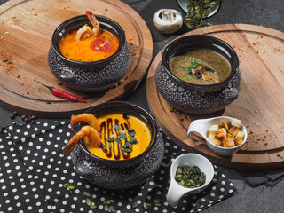 Set of soups in dark pots. Wooden desks