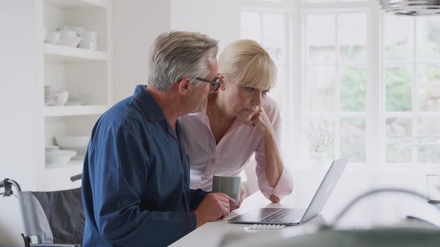 Senior Couple With Man In Wheelchair Looking Up Information About Medication Online Using Laptop