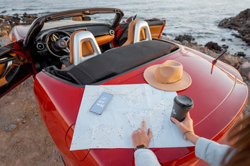Woman searching on paper map while travelnig by car near the ocean, close-up on car truk with map