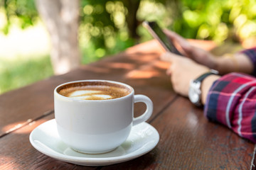 Cup of hot coffee on wooden table and women holding and using mobile