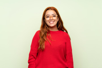 Fototapeta premium Teenager redhead girl with sweater over isolated green background with glasses