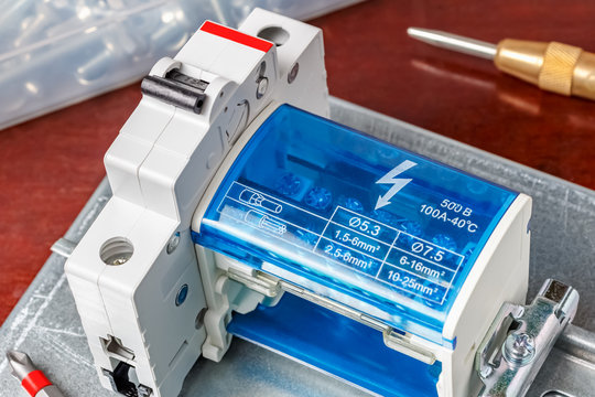 Installed automatic circuit breaker and wire terminal with closed blue transparent plastic protective cover close-up. Assembling of electrical panel in workshop