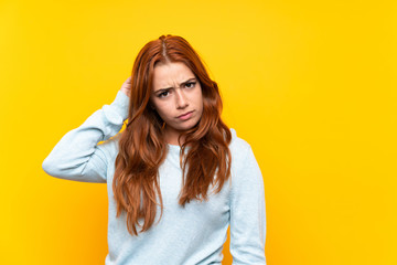 Teenager redhead girl over isolated yellow background having doubts