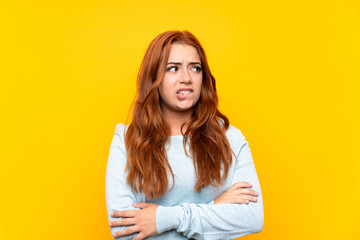 Teenager redhead girl over isolated yellow background with confuse face expression