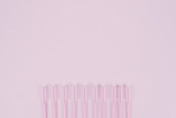 A row of disposable eyelash brushes on a pastel pink background with place for text. The concept of eyelash extension and makeup. Copyspace