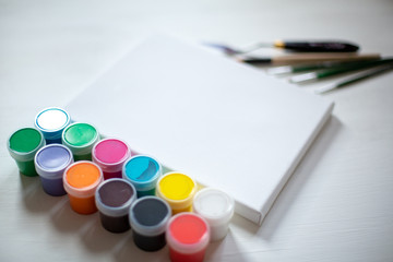 Art canvas with cans of acrylic paint and art brushes.  White canvas