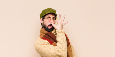 young cool bearded man feeling disgusted, holding nose to avoid smelling a foul and unpleasant...