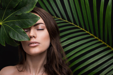 Portrait of a young beautiful woman with perfect smooth skin with a large green tropical leaf