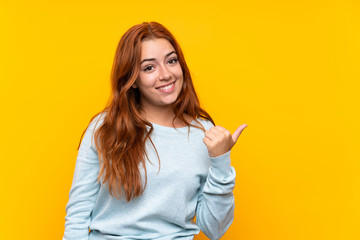 Teenager redhead girl over isolated yellow background pointing to the side to present a product