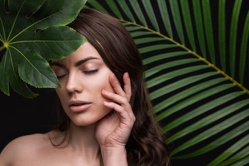 Portrait of a young beautiful woman with perfect smooth skin with a large green tropical leaf