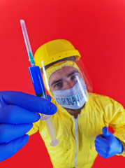 Man in yellow chemical protection suit and face protective mask  with the inscription `coronavirus`. Shoulder portrait. Red background. Without glasses. Protective helmet. Hands in blue gloves. 