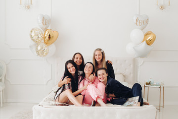 Group of happy girl friends laughing posing on bed enjoying pajamas party full shot. Smiling female...