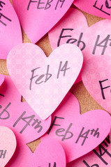 Handwritten Valentine's Day reminders for Feb 14th on pink hearts stuck to bulletin board 