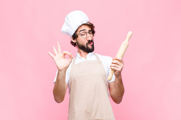 young crazy baker man with a cook tool against pink wall
