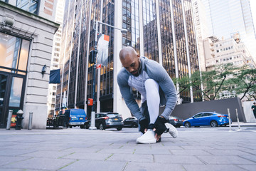 Black jogger kneeling at street and tying shoelaces