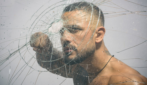 Sexy hispanic tattooed man behind broken glass. Bullet hole in glass. Destruction and crush test concept. Man style. Macho man glasscutter behind crushed glass.