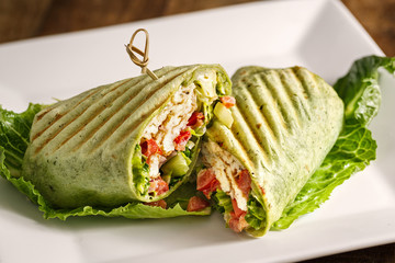 Chicken sandwich in a grilled spinach wrap served on a bed of lettuce