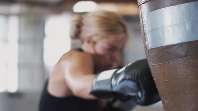 Female Boxer In Gym Training With Old Fashioned Leather Punch Bag