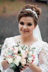 Smiling beautiful young bride. Tender bride with beautiful make up. Autumn wedding. Beauty portrait of bride wearing in wedding dress. Young attractive bride with bouquet of flowers.