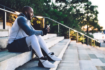 Smiling African American young sportsman sitting while listening to music and using smartphone