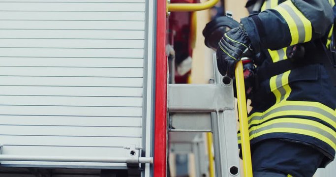 Blond young Caucasian female fireguard going up the ladder on the fire truck and looking at the side. Close up.