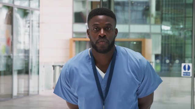 Portrait Of Male Nurse Wearing Scrubs Standing In Modern Hospital Building