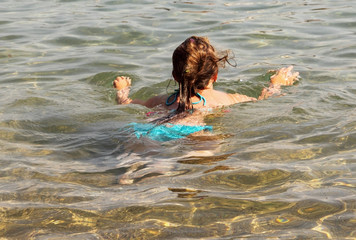 Back of girl swimming in the sea shallow.
