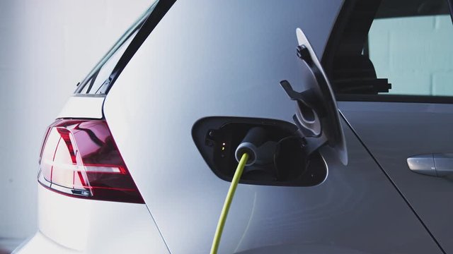 Close Up Of Hand Attaching Power Cable To Electric Car Before Taking Cloth Bags From Trunk