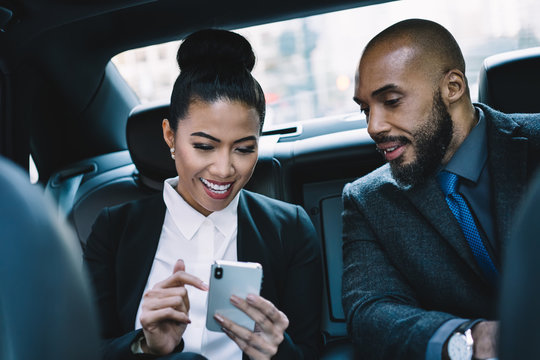 Happy businesswoman showing smartphone to colleague in car