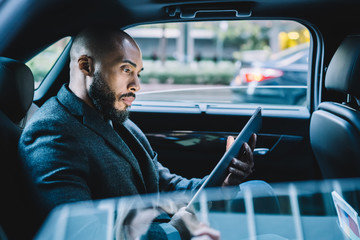 Fototapeta na wymiar Serious black businessman using tablet in car