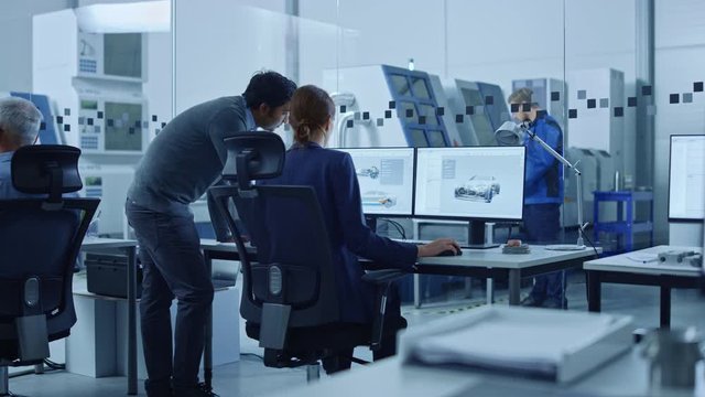 Automotive Design Factory: Project Manager and Chief Mechanical Engineer Talk, Point at Computer Display Showing 3D Electric Car Model in CAD Software. High Tech Facility with Automatic CNC Machinery