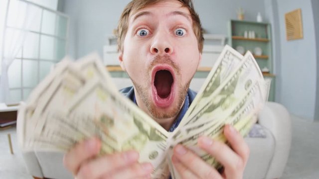 Portrait of excited young man holding bunch of money banknotes and celebrating
