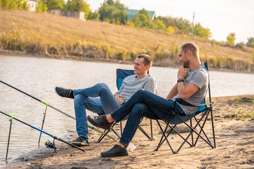 Fototapeta premium leisure and people concept. Happy friends with fishing rods on pier by lakeside.
