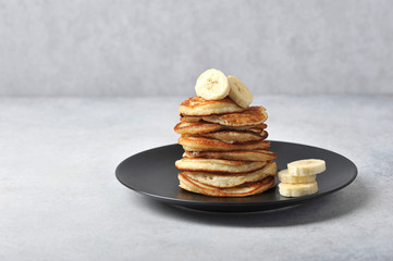A pile of fritters on a black plate.  Pancakes are decorated with banana slices.  Light background.  Free space for text.