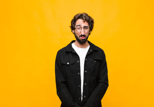 young crazy handsome man feeling sad and whiney with an unhappy look, crying with a negative and frustrated attitude against orange wall
