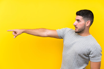 Young handsome man over isolated yellow background pointing finger to the side
