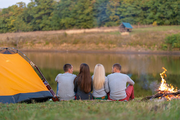 A group of friends is enjoying view, camping with bonfire on riverside