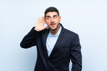 Handsome man over isolated blue background listening to something by putting hand on the ear