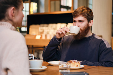 Young casual bearded man drinking coffee with girlfriend in cafe