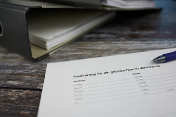 on a wooden background is lying a white German document, the first sentence means purchase contract for a used car, then the words for seller and buyer and following space for the private data