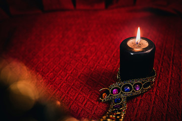 black candle lit with precious jewels decorated on red cloth, esoteric concept