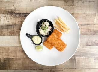 Top view of fish and chips including deep fried cod, french fries, lemon, and tartar sauce  on  wooden background