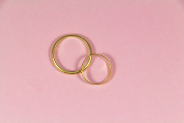 Two wedding rings made in gold on pink background