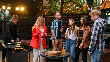 Group of young cheerful friends are enjoying a time together at a barbecue party in the cozy...